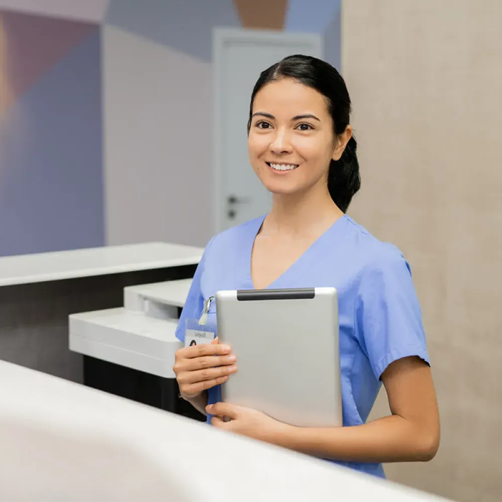 Medical assistant in front office holding tablet and smiling with patient