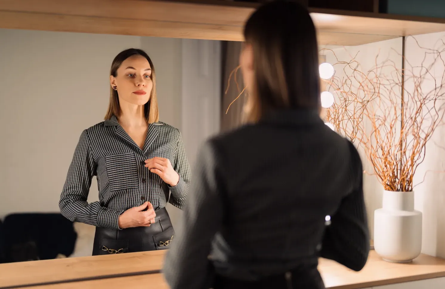 Self-confident woman looking at her reflection into the mirror indoors.